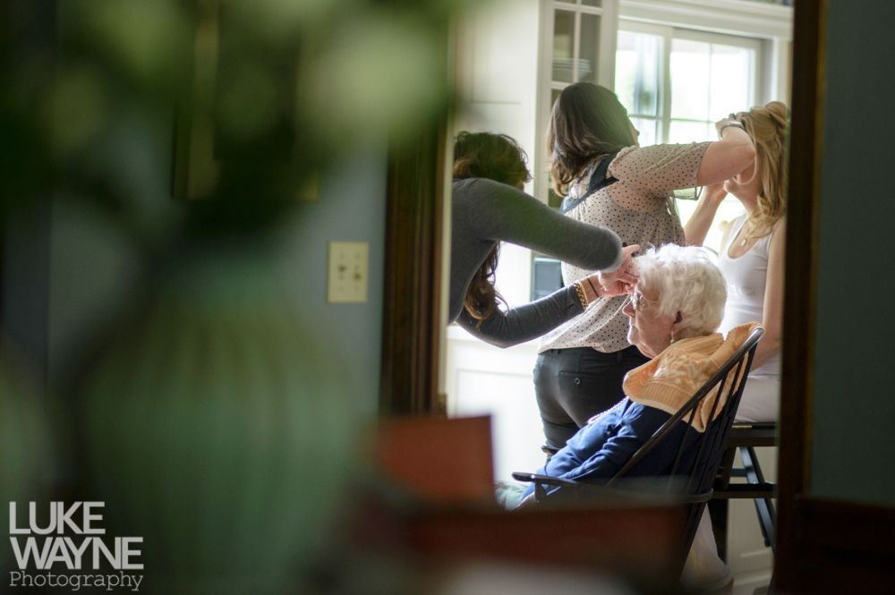 Reflection in mirror of people styling hair; an elderly person sits in a chair.