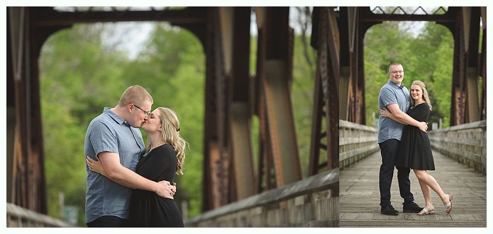 Couple kissing on a bridge; one embraces the other. Both are wearing blue and black on a sunny day.