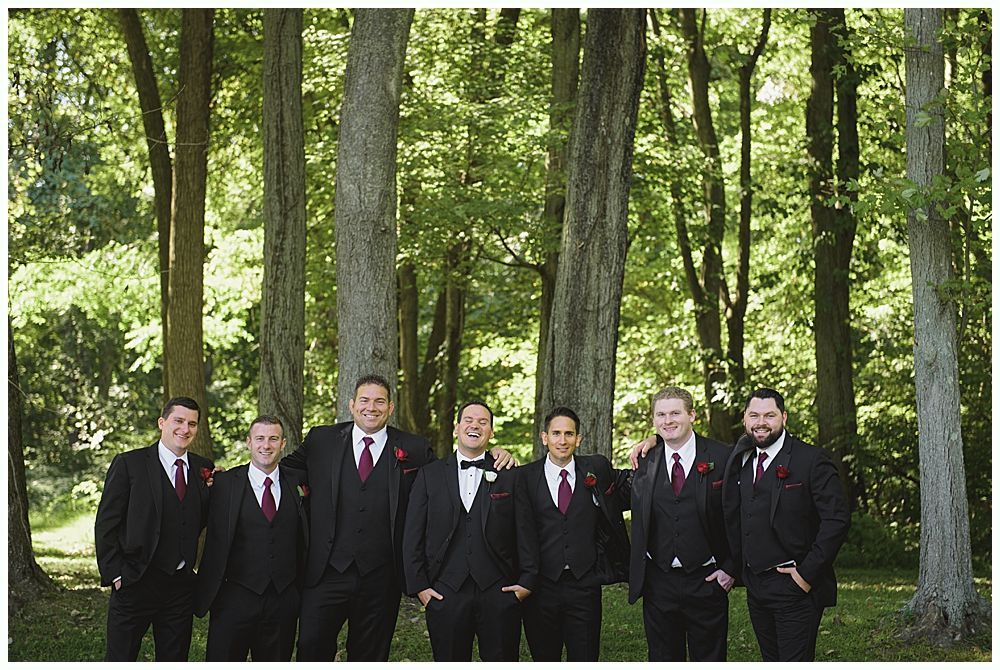 Wedding ceremony outdoors under a tree, guests seated. Couple, bridal party at altar. Autumn foliage.