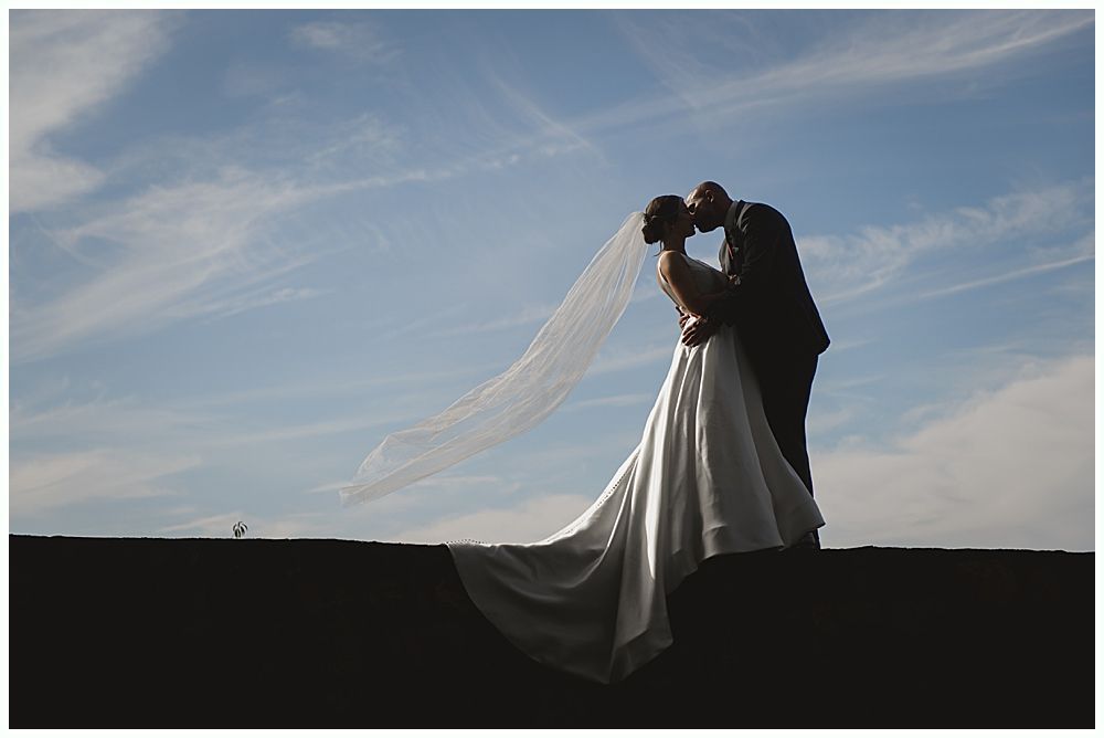 Wedding ceremony outdoors under a tree, guests seated. Couple, bridal party at altar. Autumn foliage.