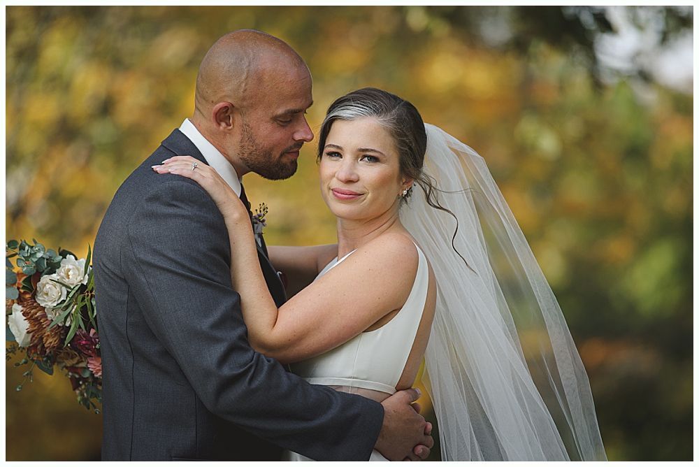 Wedding ceremony outdoors by a lake with a couple, wedding party, and guests under a cloudy sky.