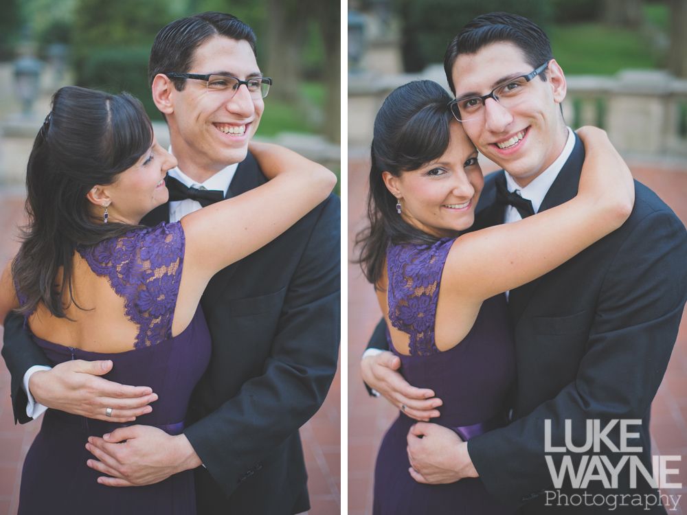 Couple embracing, smiling. Woman in purple dress with lace back, man in black suit and bow tie. Outdoors.