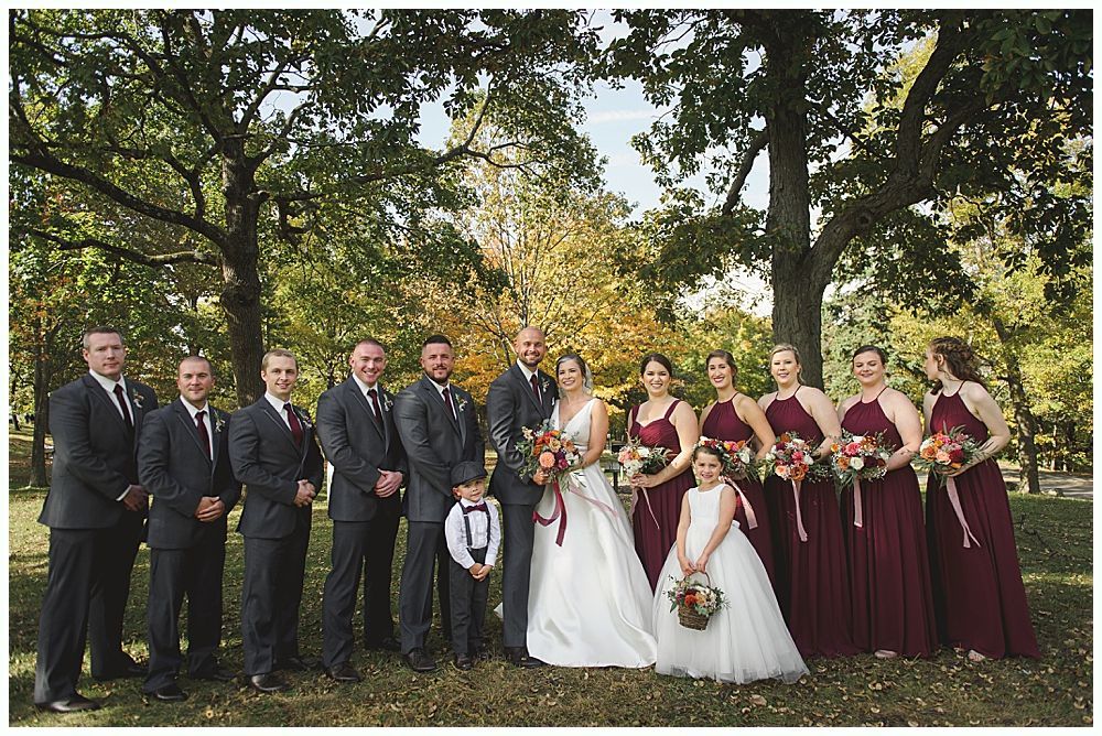 Wedding ceremony: Couple kissing at altar under weeping willow tree; bridal party and guests watching.