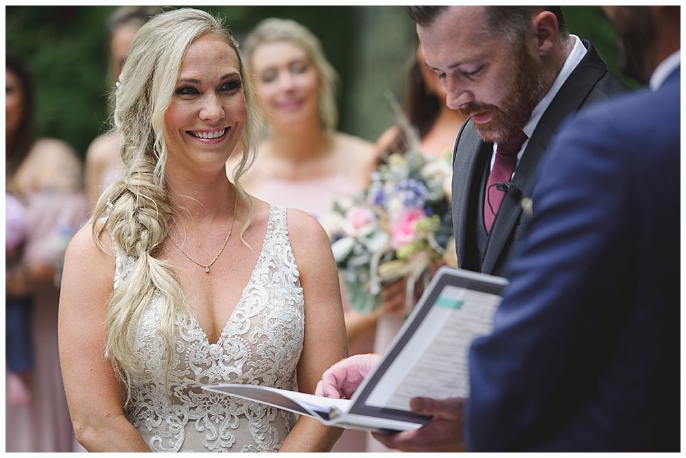 Bride in a white wedding dress smiles, looking over her shoulder as her veil blows in the wind outdoors.