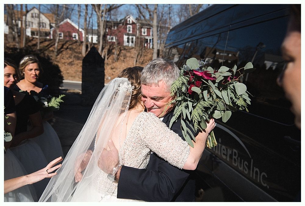 Bride in a white wedding dress smiles, looking over her shoulder as her veil blows in the wind outdoors.