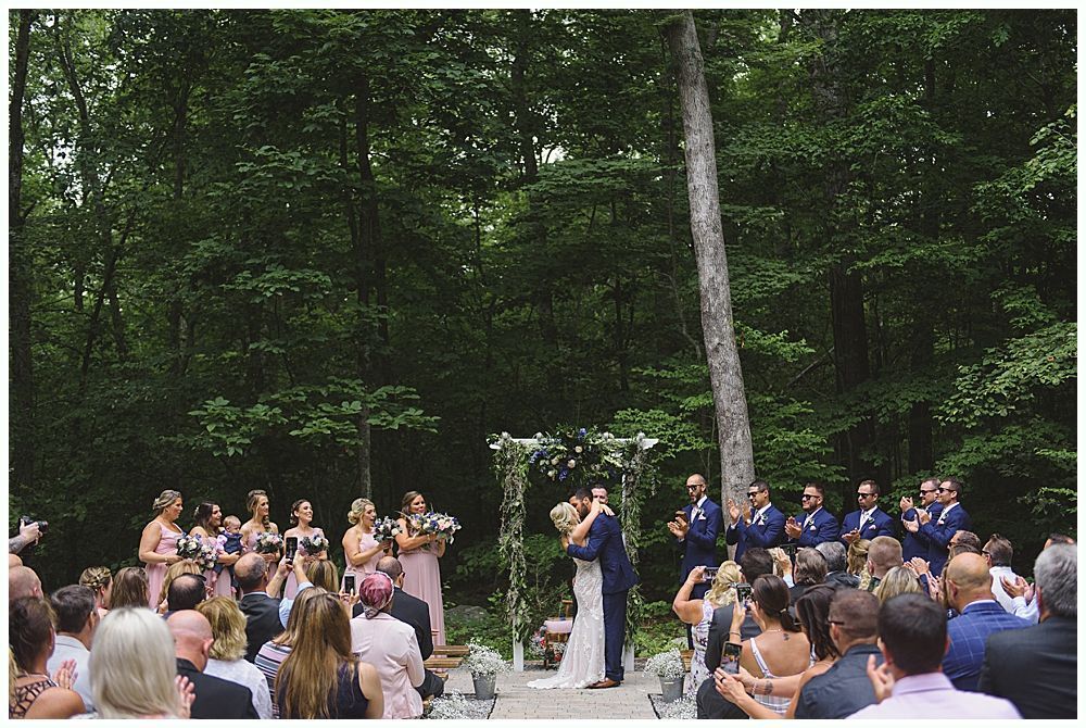 Wedding party walking on a grassy lawn; bride and groom in center, bridesmaids in red, groomsmen in navy.