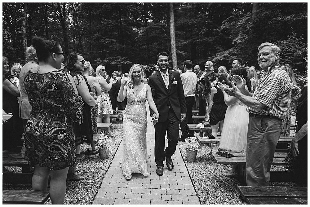 Wedding party smiling outdoors near water. Bride and bridesmaids in red, groom and groomsmen in navy.