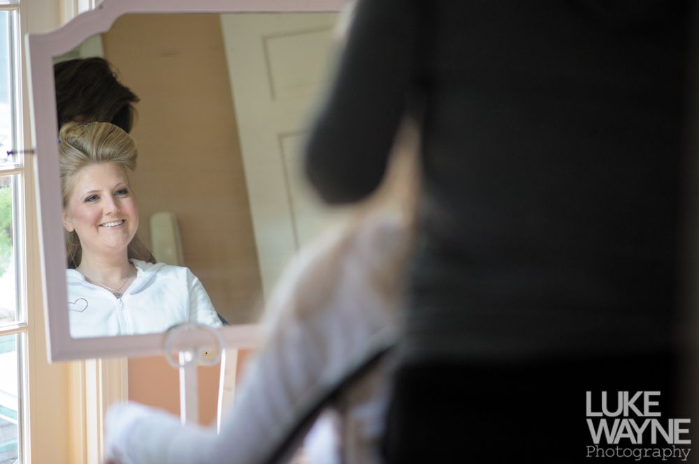 Woman smiling at herself in a mirror, getting her hair done. Inside, light room.