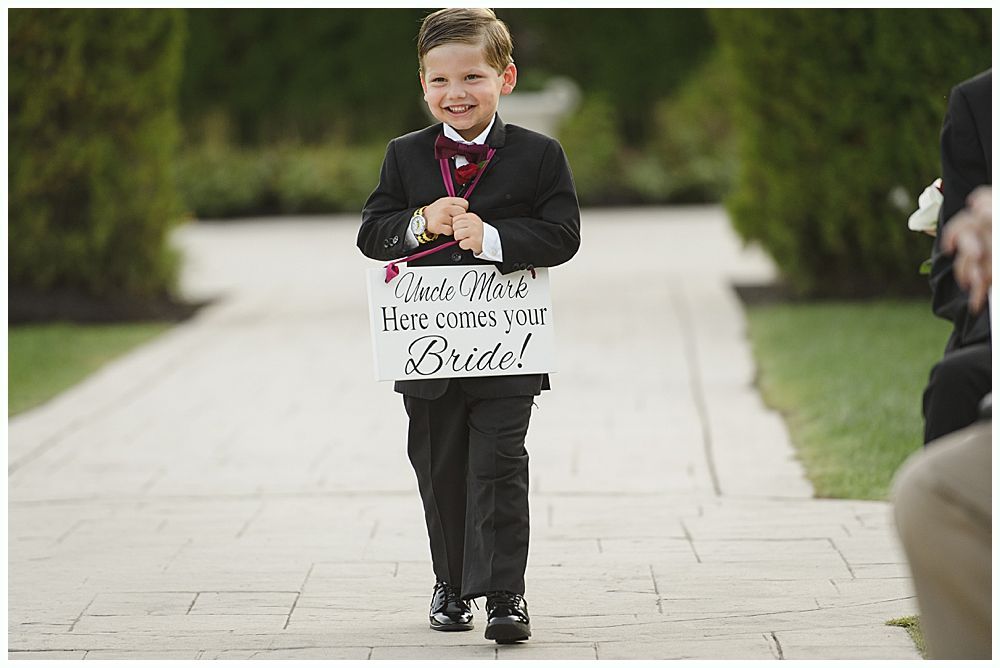 Bride and groom walk hand-in-hand across a grassy hilltop; black and white photograph with a cloudy sky backdrop.