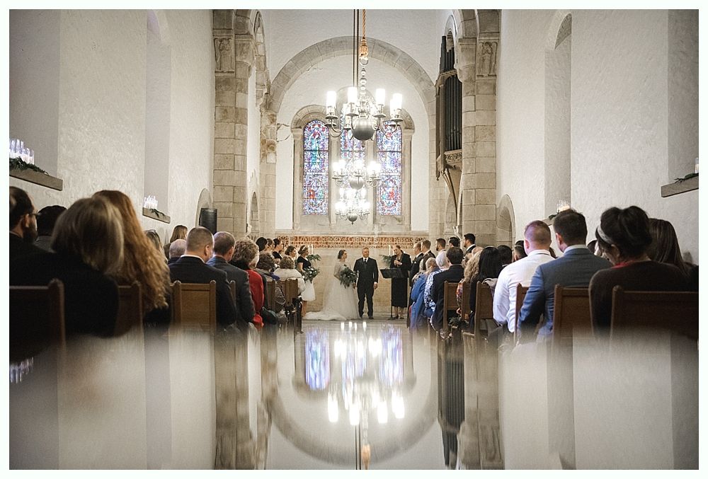 Bride and groom kiss under a weeping willow tree, backlit by sunlight.