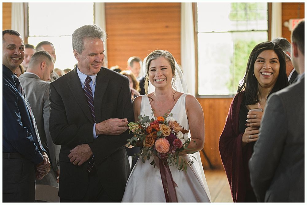 Bride and groom walk hand-in-hand across a grassy hilltop; black and white photograph with a cloudy sky backdrop.