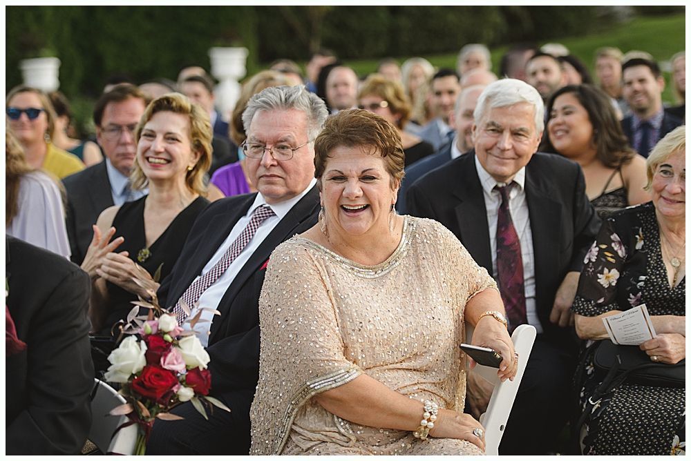 Bride touches groom's face; he holds a bouquet. They smile outdoors.