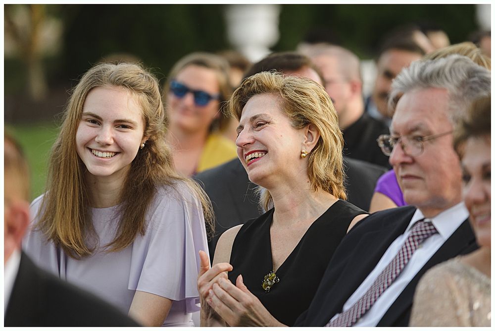 Bride and groom kiss under a weeping willow tree, backlit by sunlight.