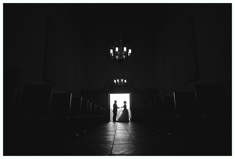Woman in red gown throws bouquet at wedding reception. Man in suit reaches for it. Wooden interior.
