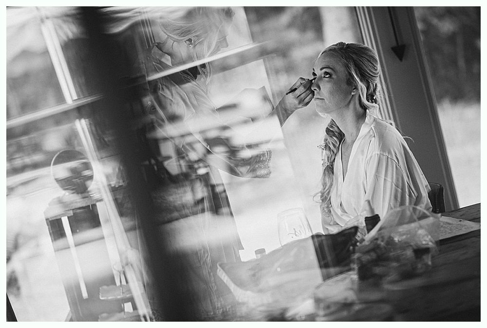 Woman putting on earrings, smiling. Dark background, wearing wedding dress.