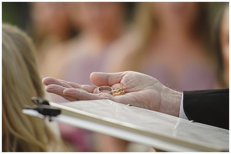 Woman in red gown throws bouquet at wedding reception. Man in suit reaches for it. Wooden interior.