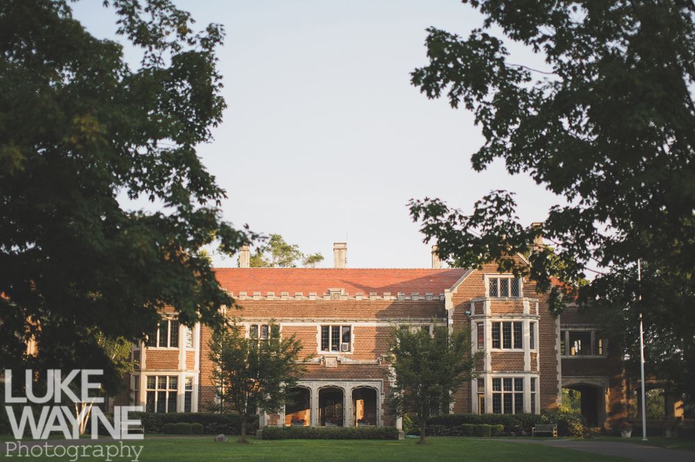 Large brick building framed by trees, with a red tile roof and arched entrance.