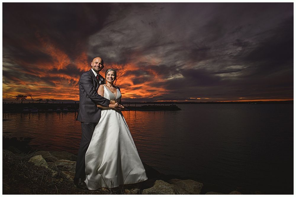 Woman in red gown throws bouquet at wedding reception. Man in suit reaches for it. Wooden interior.