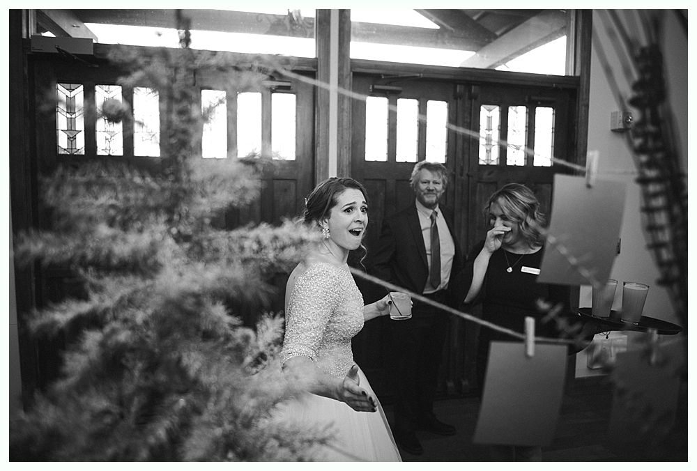 Woman in red dress giving a speech at a wedding. Bride smiles. Wooden interior.