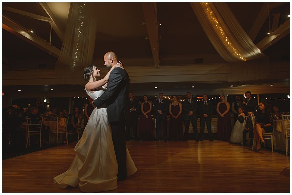 Couple dances at a wedding reception; chandelier and string lights in background.