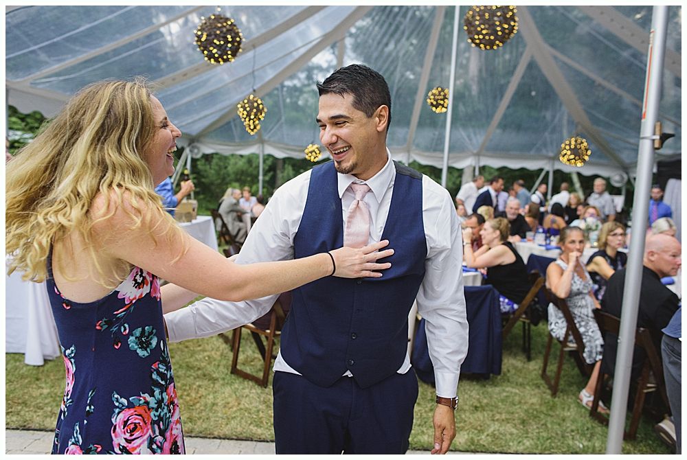Woman laughs at a formal dinner, seated next to a smiling man with a yellow tie; table setting.