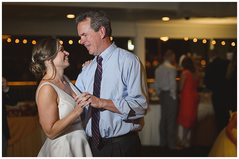 Woman in red dress giving a speech at a wedding. Bride smiles. Wooden interior.