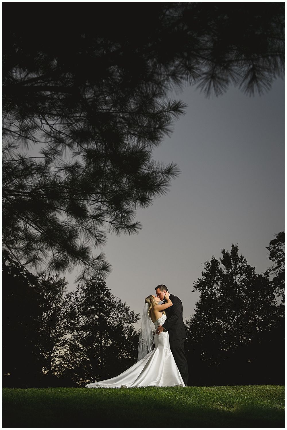 A man in a suit gives a speech at a wedding. The bride and groom laugh while listening.