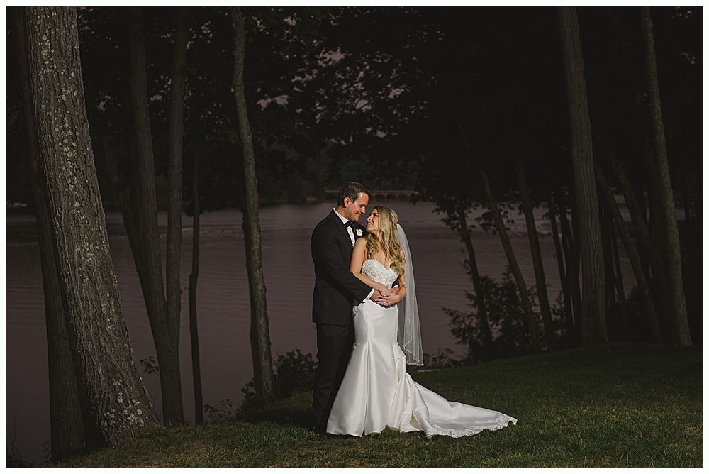 Wedding couple laughing during a reception. The groom covers his face, and the bride smiles widely.