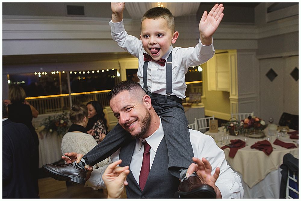 Wedding couple laughing during a reception. The groom covers his face, and the bride smiles widely.