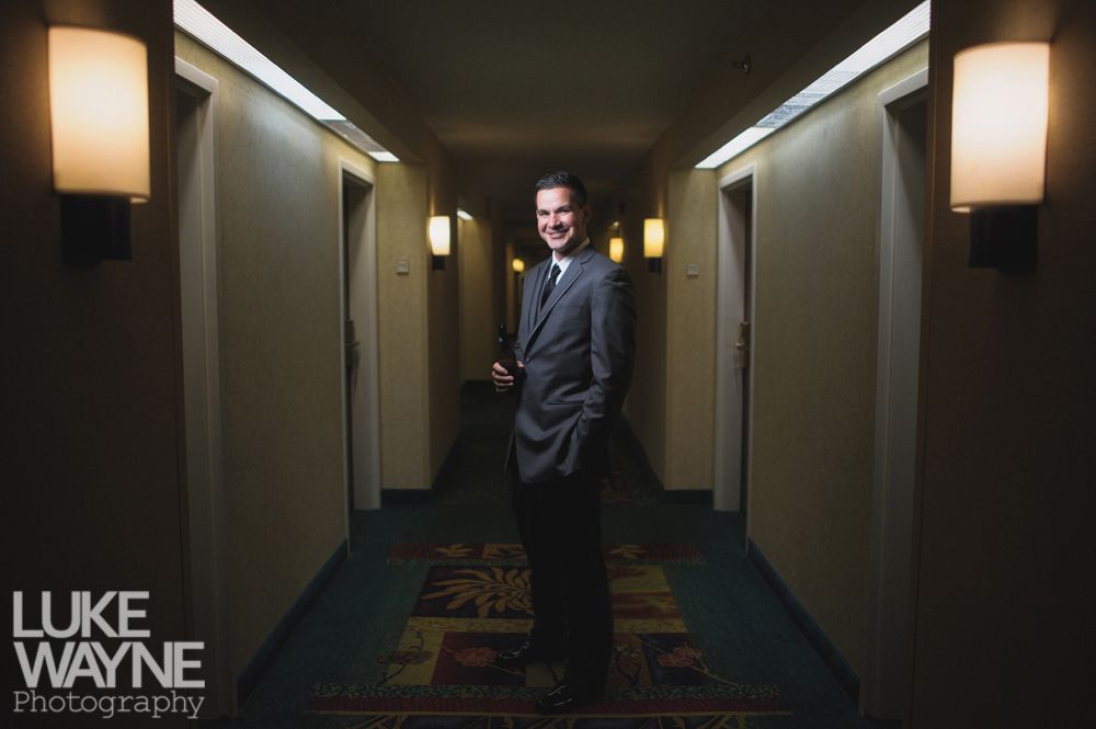 Man in suit stands in hotel hallway, smiling.