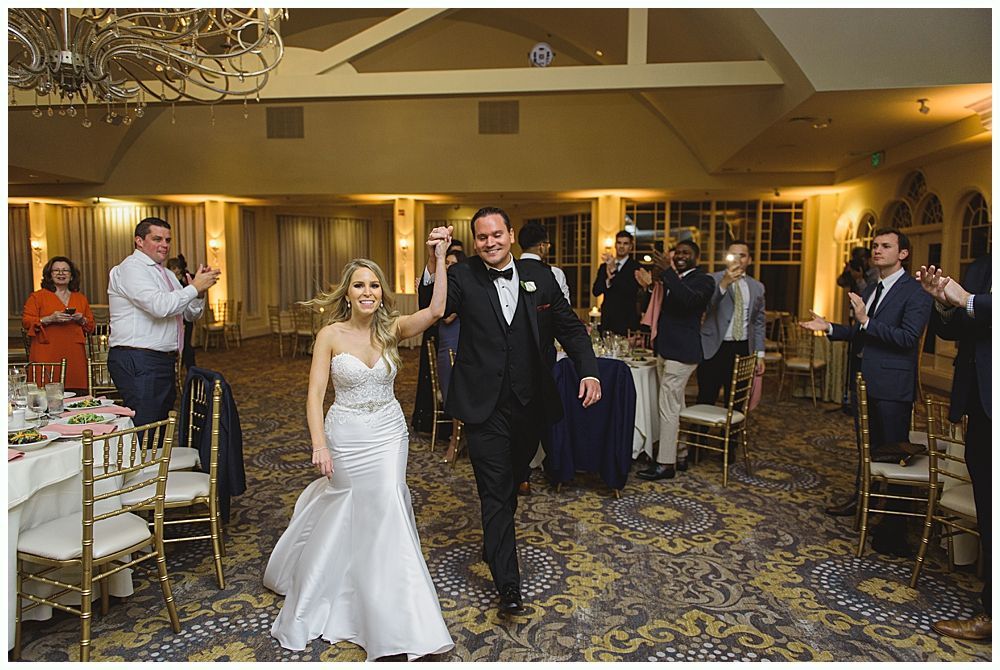 Woman hugs boy wearing a tie and blazer in a warmly lit room. Both smile.