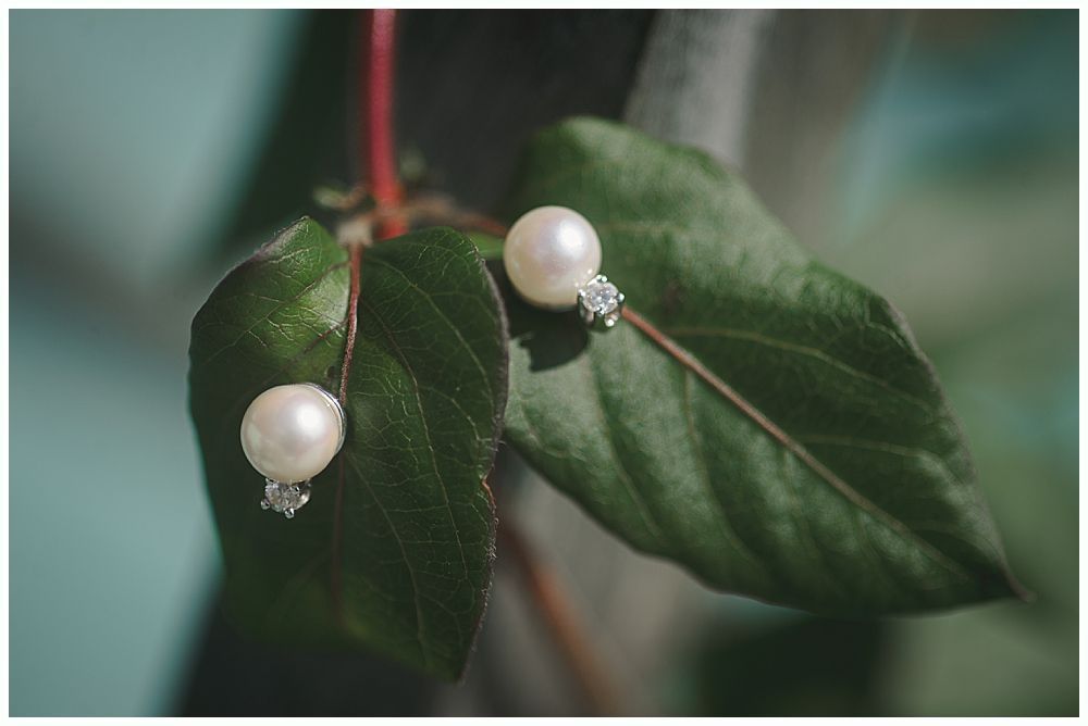 Bride holding bouquet; burgundy, cream, and green flowers. She looks down, lit by soft light.