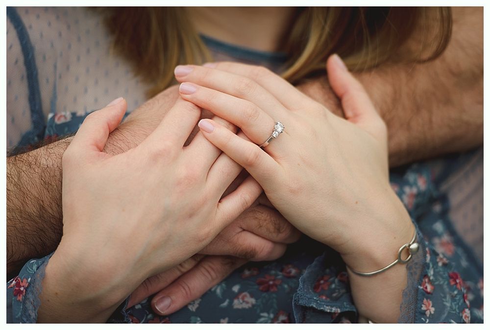 Bride holding bouquet; burgundy, cream, and green flowers. She looks down, lit by soft light.