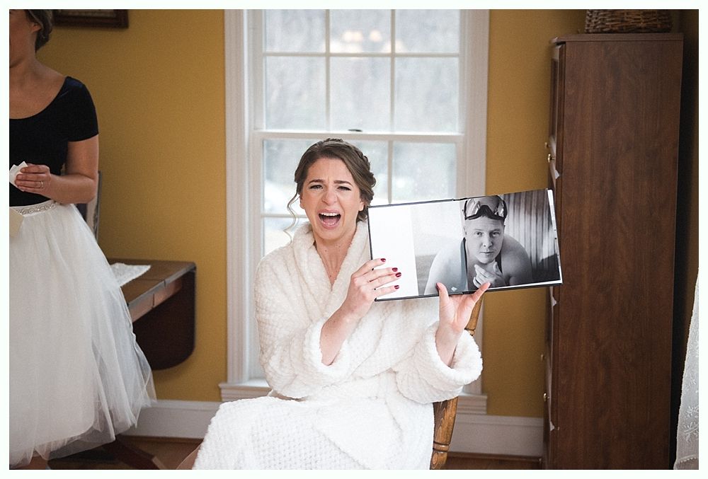 Bride holding bouquet; burgundy, cream, and green flowers. She looks down, lit by soft light.