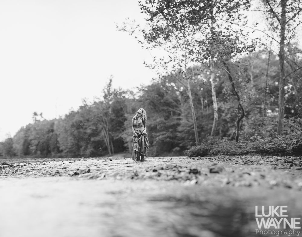 Black and white landscape with a dark, cloudy sky over a field. Sunbeams filter through the clouds.