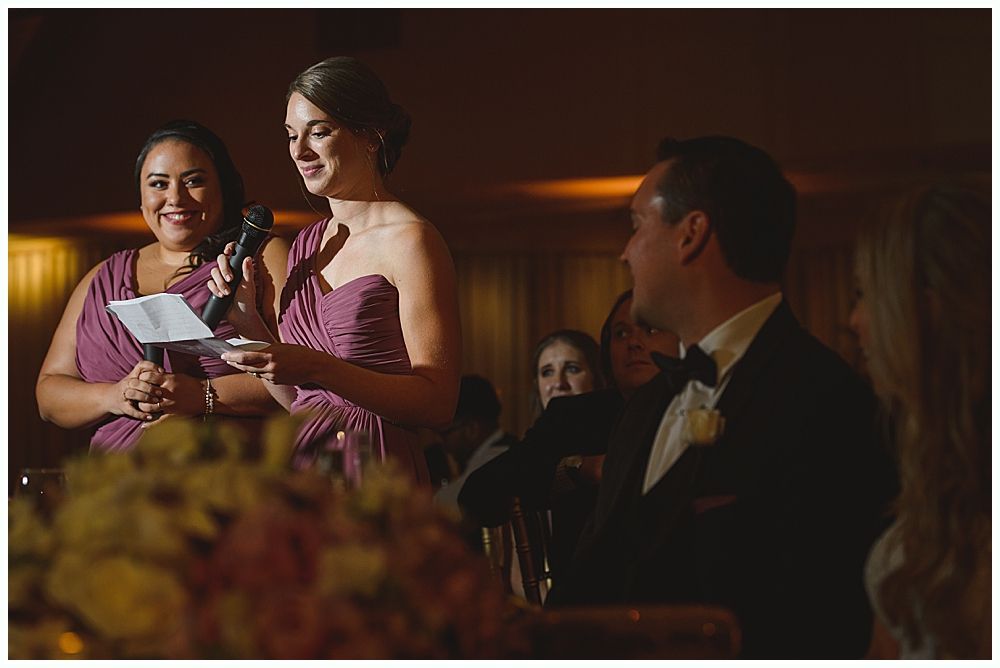 Bride and groom embrace outdoors, veil billowing, wedding bouquets visible.