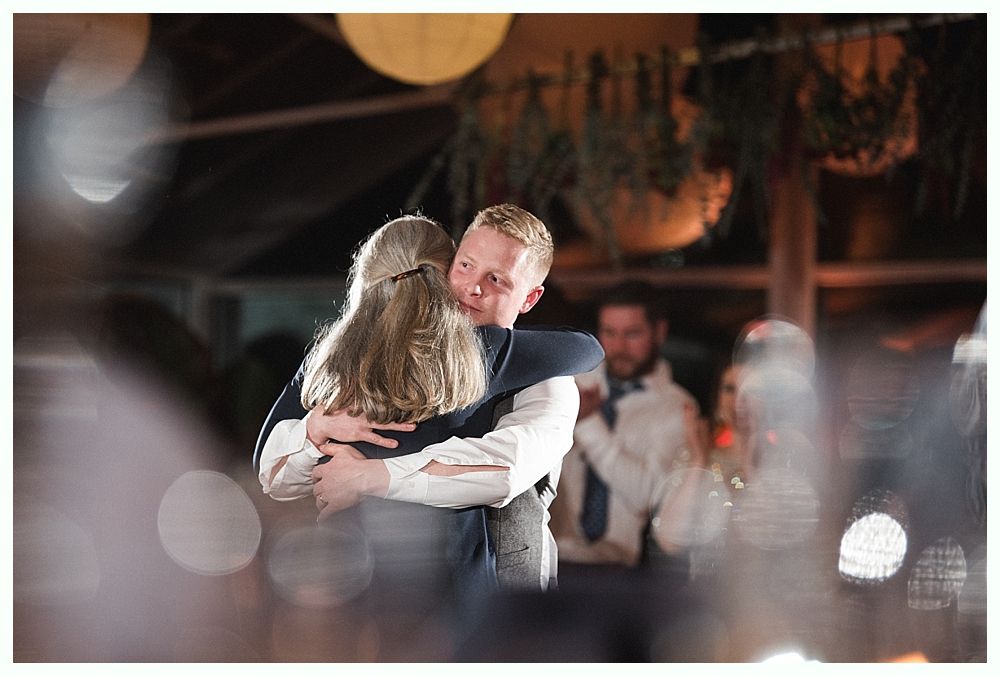 Wedding cake with figurines, on a wood slice. Rustic decor with blurred lights in the background.