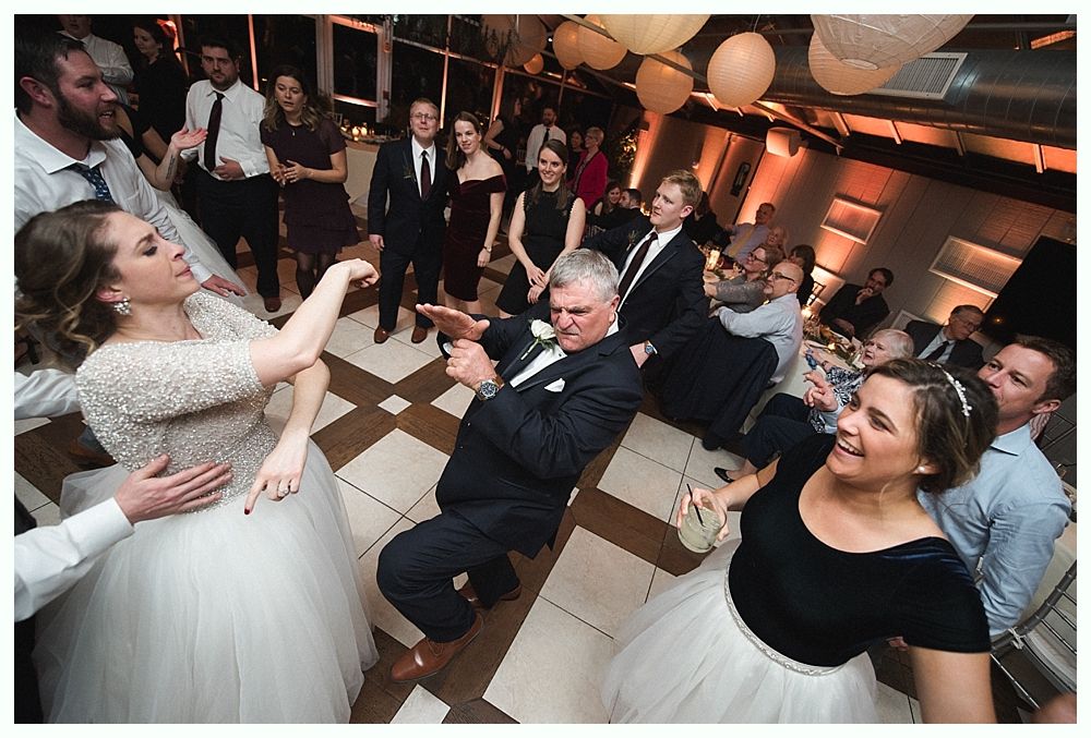 Wedding cake with figurines, on a wood slice. Rustic decor with blurred lights in the background.
