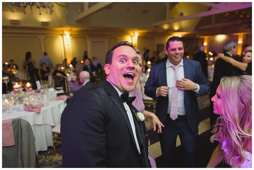 Bride and groom embrace outdoors, veil billowing, wedding bouquets visible.