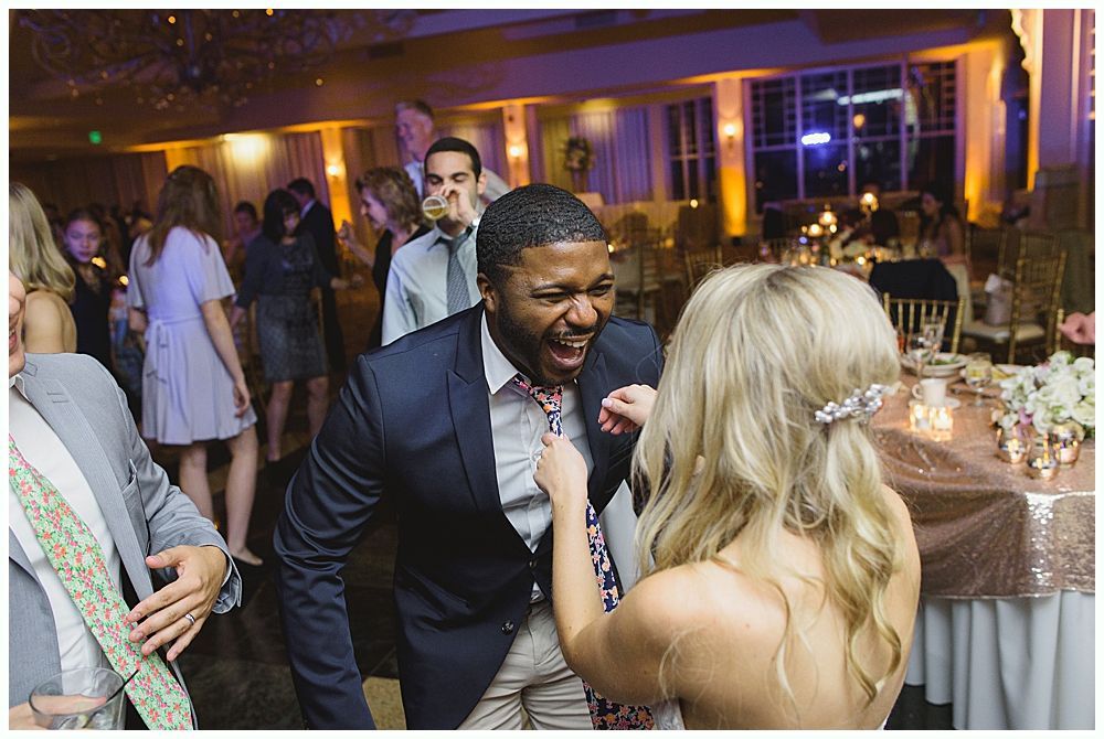 Bride and groom embrace outdoors, veil billowing, wedding bouquets visible.