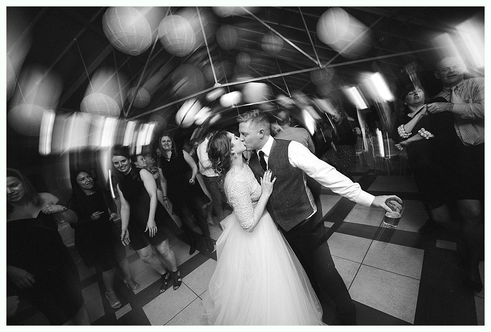 Wedding cake with figurines, on a wood slice. Rustic decor with blurred lights in the background.