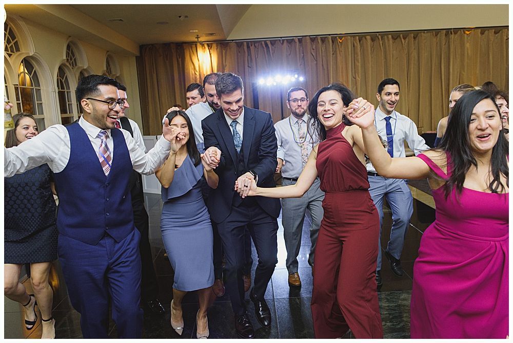 Bride and groom embrace outdoors, veil billowing, wedding bouquets visible.