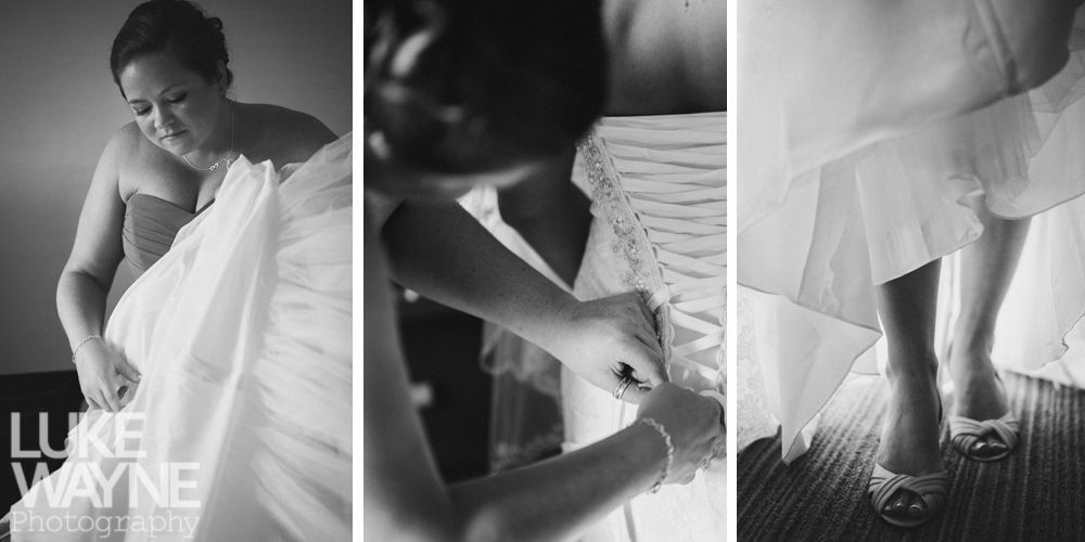 A bride is helped into her wedding dress. A bridesmaid fastens the corset back. The bride's shoes are visible.