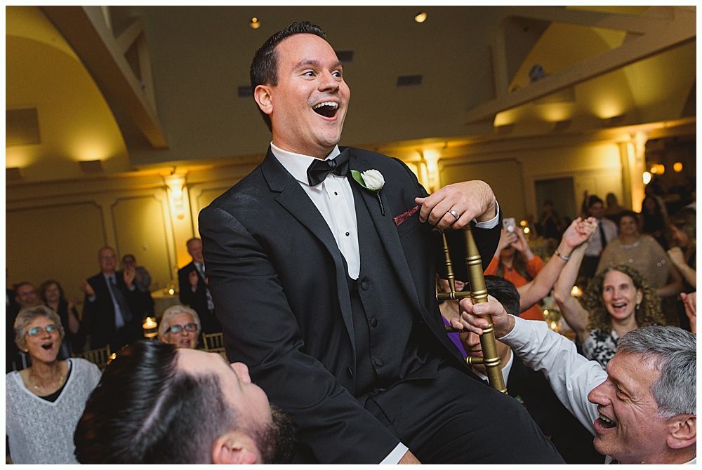 Bride and groom embrace outdoors, veil billowing, wedding bouquets visible.