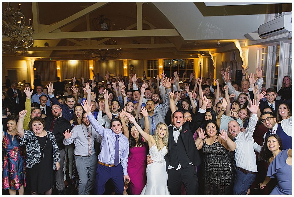 Bride and groom embrace outdoors, veil billowing, wedding bouquets visible.