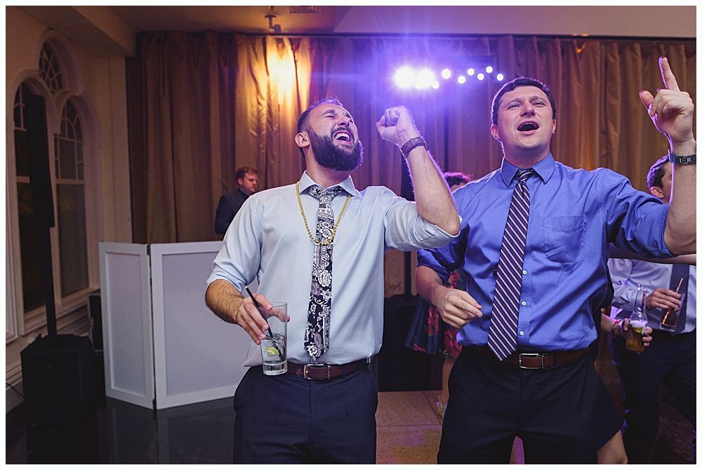 Bride and groom embrace outdoors, veil billowing, wedding bouquets visible.