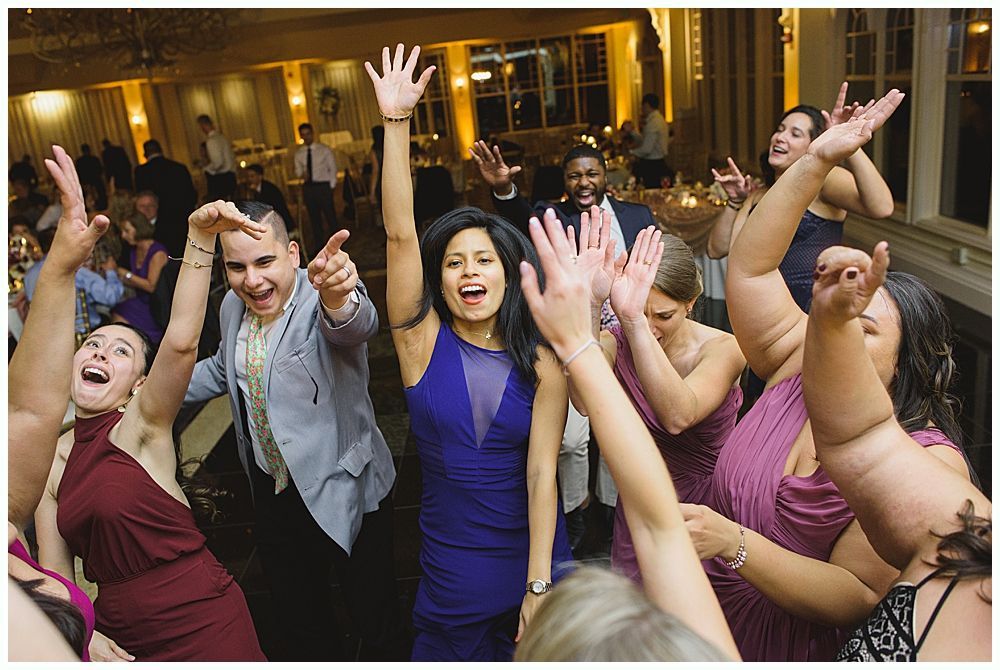 Bride and groom embrace outdoors, veil billowing, wedding bouquets visible.