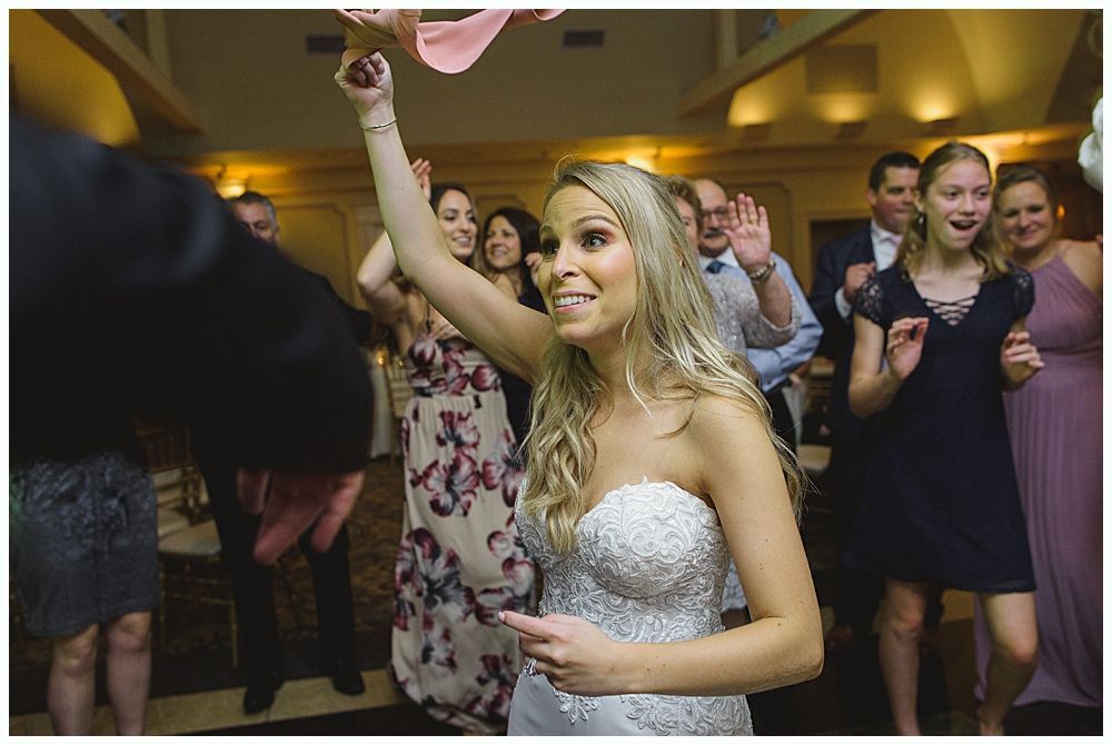 Bride and groom embrace outdoors, veil billowing, wedding bouquets visible.