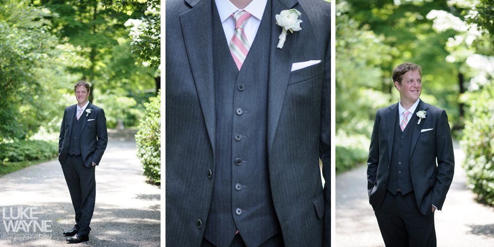 Man in dark suit with pink tie, flower, and pocket square on a pathway with trees.