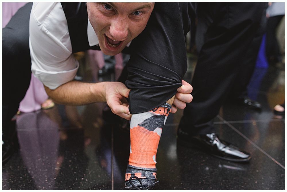 Bride and groom embrace outdoors, veil billowing, wedding bouquets visible.